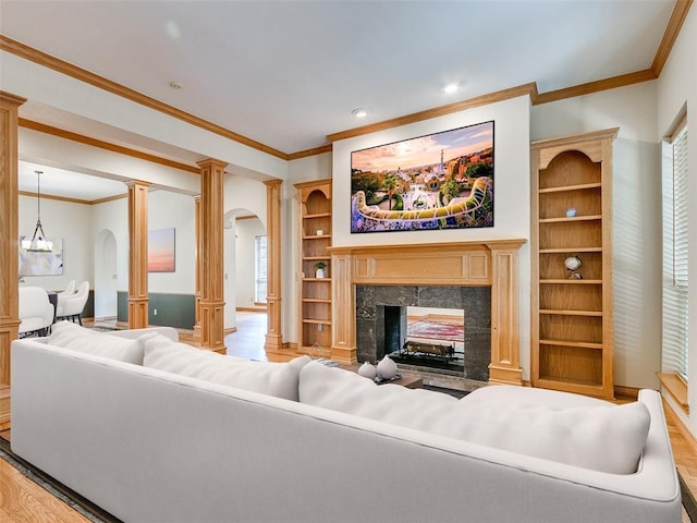 living area featuring built in shelves, crown molding, a fireplace, wood finished floors, and an inviting chandelier