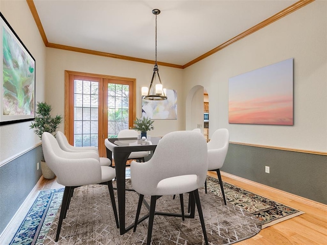 dining space with arched walkways, crown molding, wood finished floors, a chandelier, and baseboards