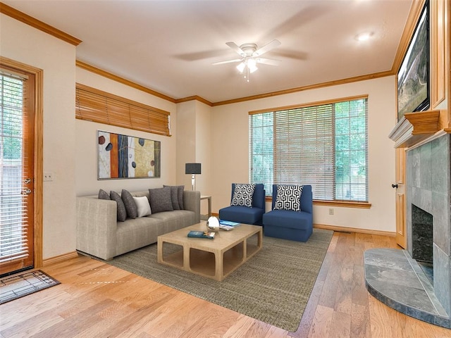 living room with ceiling fan, wood finished floors, baseboards, a tiled fireplace, and crown molding