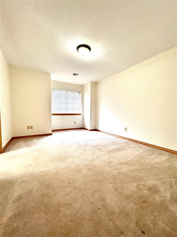 carpeted spare room featuring a textured ceiling, visible vents, and baseboards