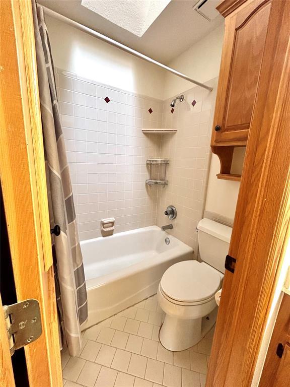 bathroom with tile patterned flooring, a textured ceiling, toilet, and shower / bath combo with shower curtain