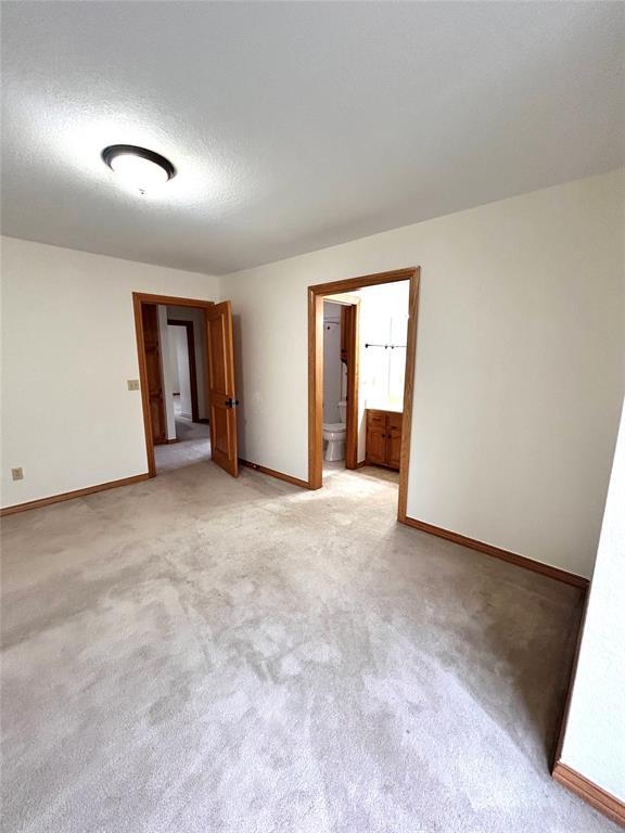 unfurnished room featuring a textured ceiling, light colored carpet, and baseboards