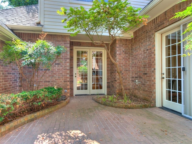 entrance to property with brick siding, a shingled roof, and french doors