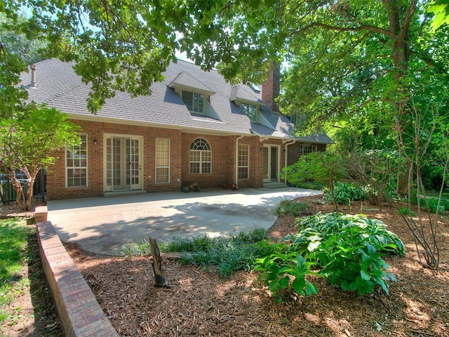 rear view of house featuring a patio, a chimney, roof with shingles, french doors, and brick siding