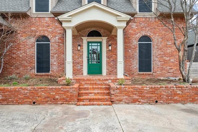 entrance to property with brick siding, mansard roof, and roof with shingles