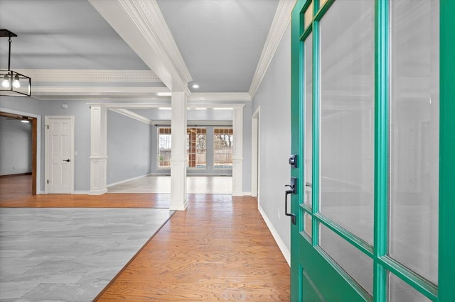 foyer entrance with decorative columns, crown molding, baseboards, and wood finished floors