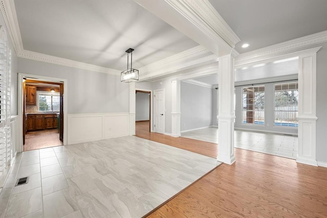 empty room with light wood-type flooring, a wainscoted wall, decorative columns, and visible vents