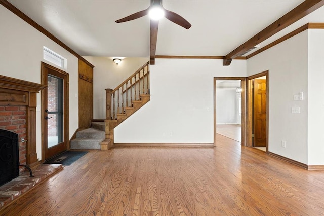 unfurnished living room with plenty of natural light, baseboards, stairway, wood finished floors, and beam ceiling