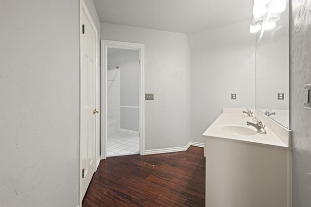 bathroom featuring double vanity, wood finished floors, a sink, and baseboards