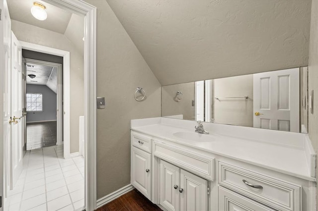 bathroom with baseboards, tile patterned floors, vaulted ceiling, a textured ceiling, and vanity