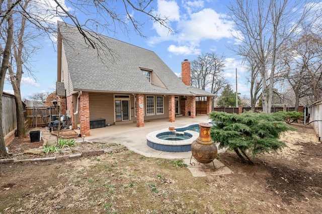 rear view of house featuring brick siding, a chimney, a patio area, an in ground hot tub, and a fenced backyard