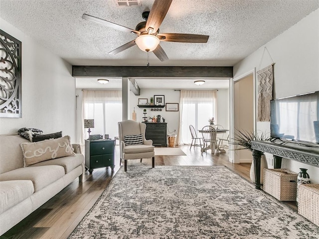 living room featuring visible vents, ceiling fan, wood finished floors, beamed ceiling, and a textured ceiling