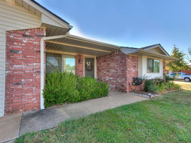 doorway to property featuring a lawn and brick siding