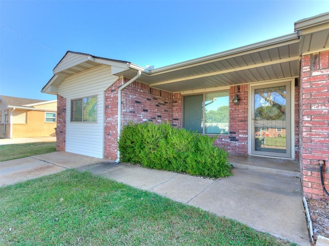 view of exterior entry featuring brick siding and a lawn