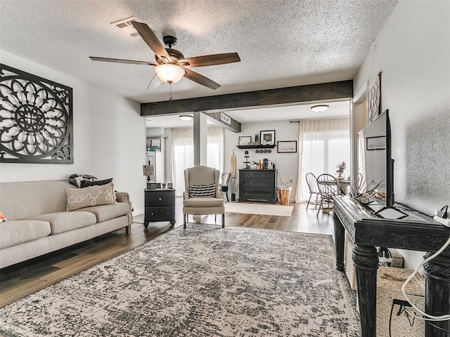 living area featuring ceiling fan, a textured ceiling, wood finished floors, and beamed ceiling