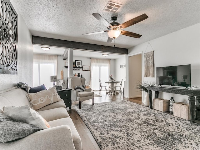 living room with a textured ceiling, wood finished floors, visible vents, and a ceiling fan