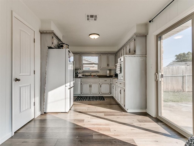 kitchen featuring a sink, visible vents, wood finished floors, freestanding refrigerator, and dark countertops