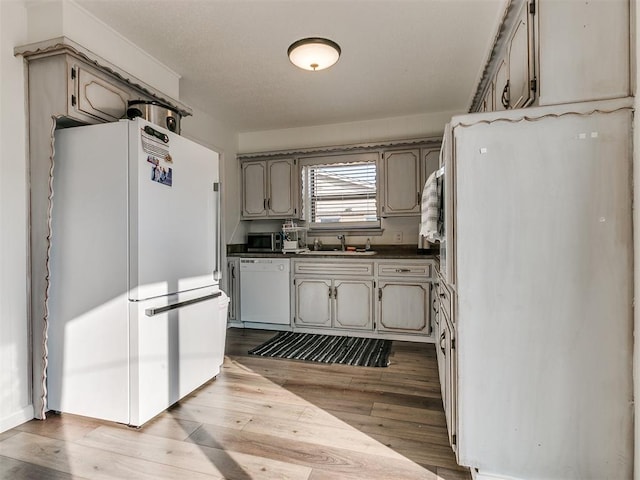 kitchen with wood finished floors, white appliances, dark countertops, and a sink