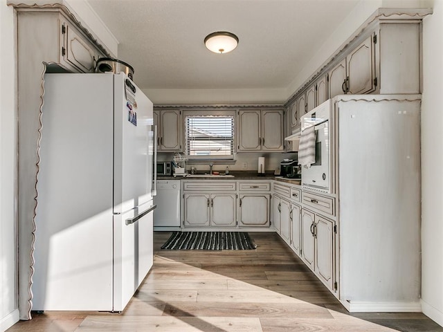 kitchen with a sink, wood finished floors, freestanding refrigerator, dishwasher, and dark countertops