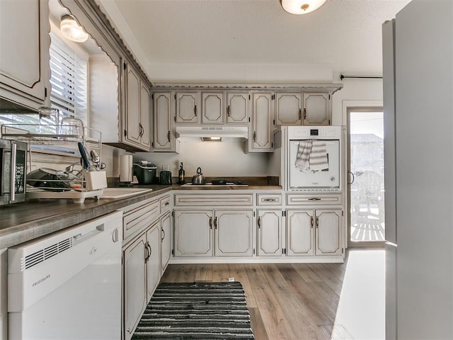 kitchen featuring light wood finished floors, white appliances, dark countertops, and under cabinet range hood