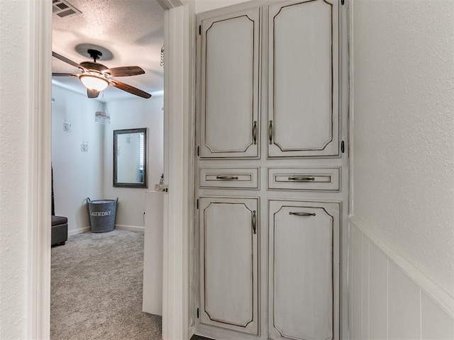 interior space featuring carpet floors, a wainscoted wall, visible vents, a ceiling fan, and a textured ceiling