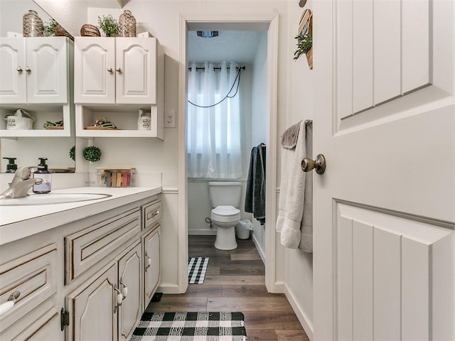 bathroom with toilet, baseboards, wood finished floors, and vanity