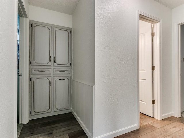 corridor featuring light wood-type flooring, wainscoting, and baseboards