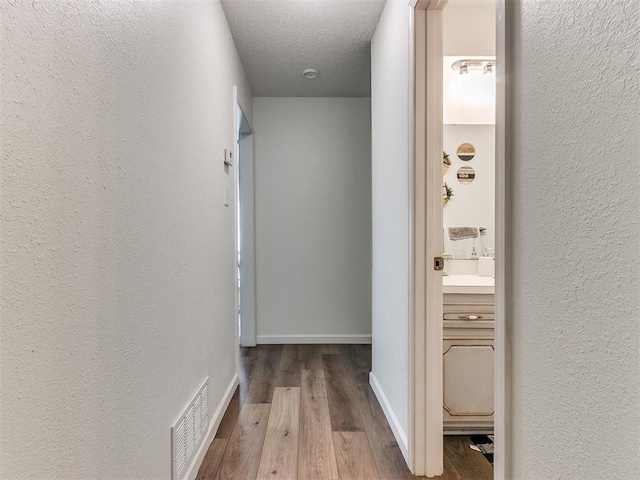 corridor with visible vents, a textured wall, a textured ceiling, wood finished floors, and baseboards