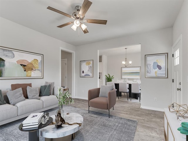 living room featuring ceiling fan with notable chandelier, baseboards, and wood finished floors