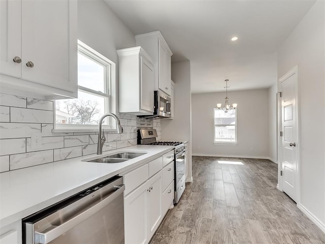 kitchen featuring stainless steel appliances, a sink, white cabinetry, tasteful backsplash, and plenty of natural light