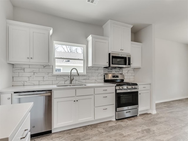 kitchen featuring stainless steel appliances, a sink, white cabinets, light countertops, and tasteful backsplash