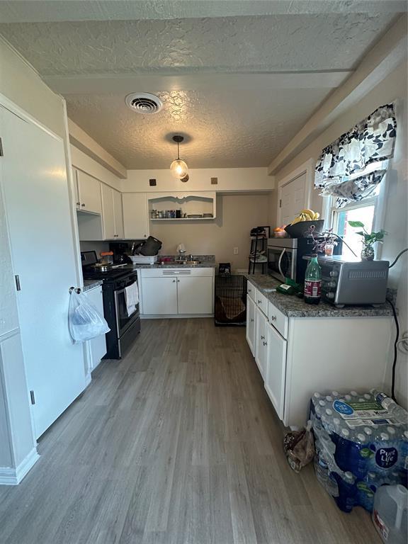 kitchen with gas range oven, visible vents, white cabinets, and wood finished floors