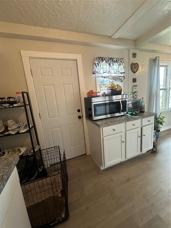 kitchen with white cabinetry, a textured ceiling, stainless steel microwave, and wood finished floors