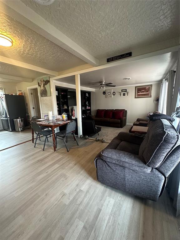 living room with a ceiling fan, beam ceiling, a textured ceiling, and wood finished floors