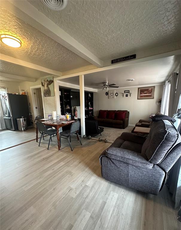 living room featuring a textured ceiling, ceiling fan, visible vents, light wood-style floors, and beam ceiling