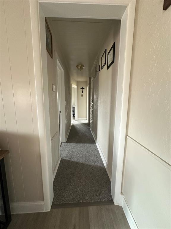 hallway featuring baseboards, wood finished floors, and a textured wall