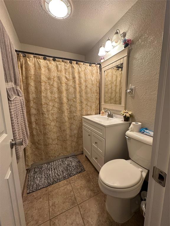 full bath with a textured ceiling, a textured wall, tile patterned flooring, toilet, and vanity