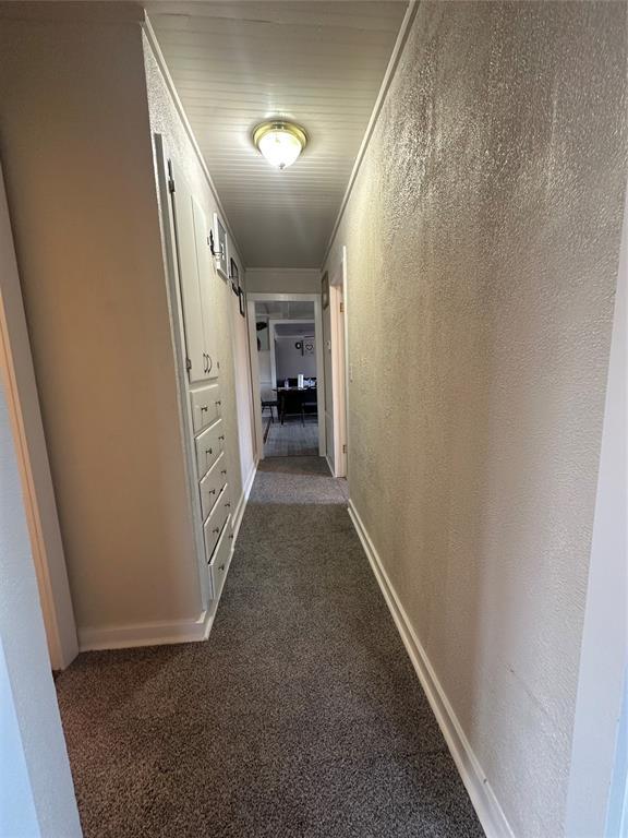 corridor featuring baseboards, a textured wall, dark carpet, and crown molding