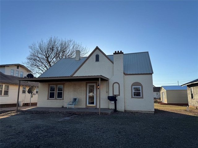 view of front of property with metal roof, a chimney, a patio area, and stucco siding