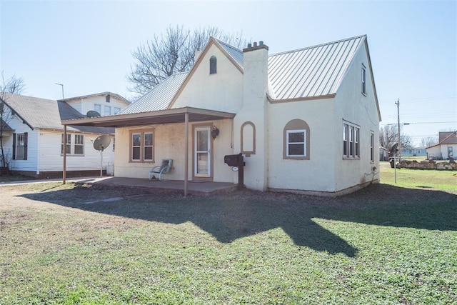 709 S Broadway, Geary, OK 73040 - rear view of house featuring a lawn, stucco siding, a chimney, metal roof, and a patio