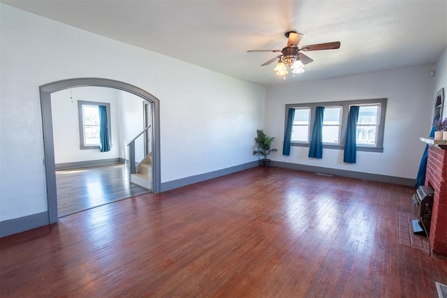 709 S Broadway, Geary, OK 73040 - unfurnished room with hardwood / wood-style floors, a fireplace, arched walkways, ceiling fan, and stairs