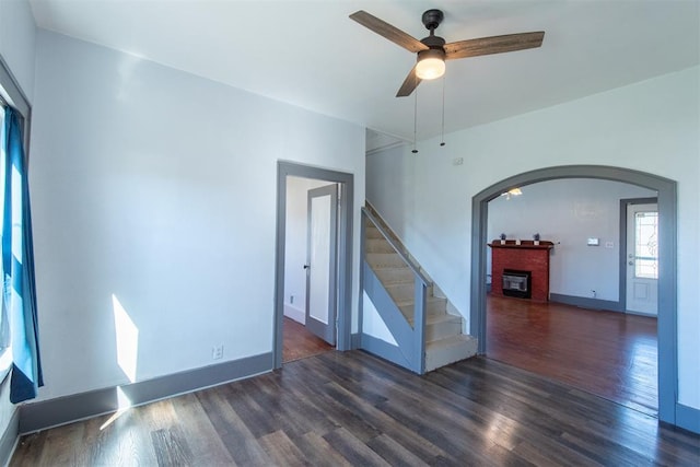 709 S Broadway, Geary, OK 73040 - spare room featuring a brick fireplace, ceiling fan, stairway, wood finished floors, and arched walkways