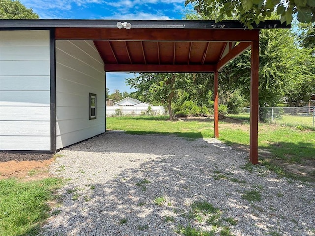 view of parking / parking lot with a carport, gravel driveway, and fence