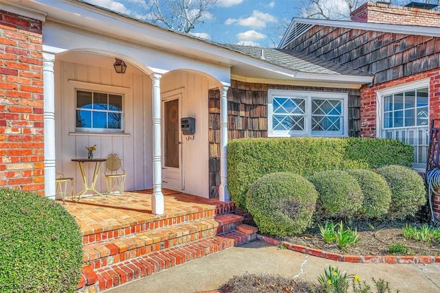 view of exterior entry featuring a porch and brick siding