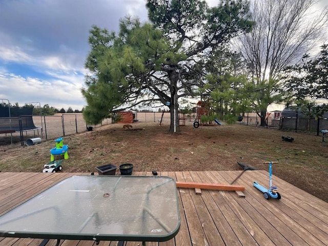 wooden deck with a trampoline, a playground, and fence