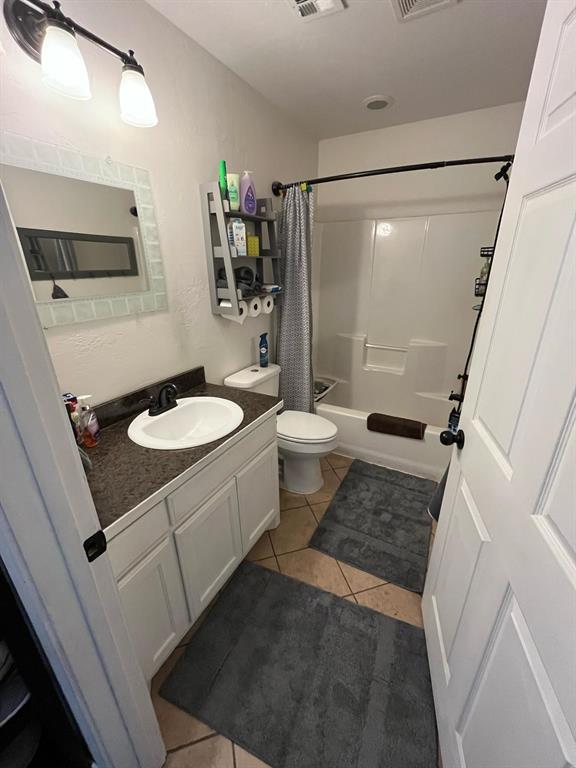 bathroom featuring visible vents, toilet, shower / bath combo with shower curtain, vanity, and tile patterned floors