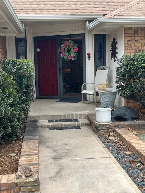 property entrance featuring covered porch, roof with shingles, and brick siding