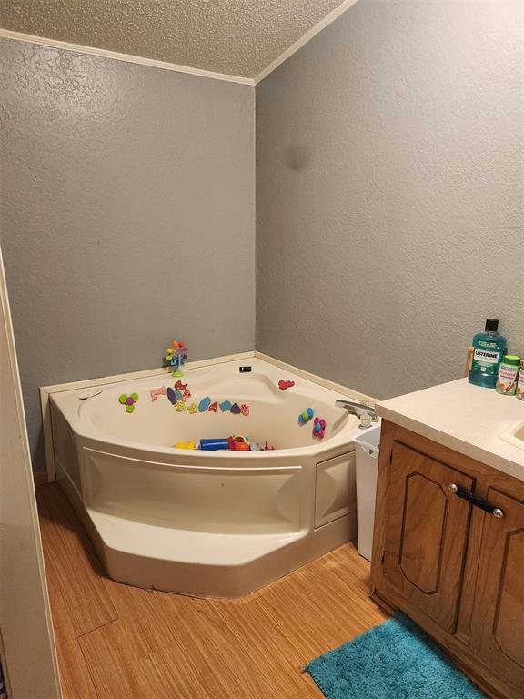 full bathroom featuring a textured wall, wood finished floors, vanity, ornamental molding, and a bath