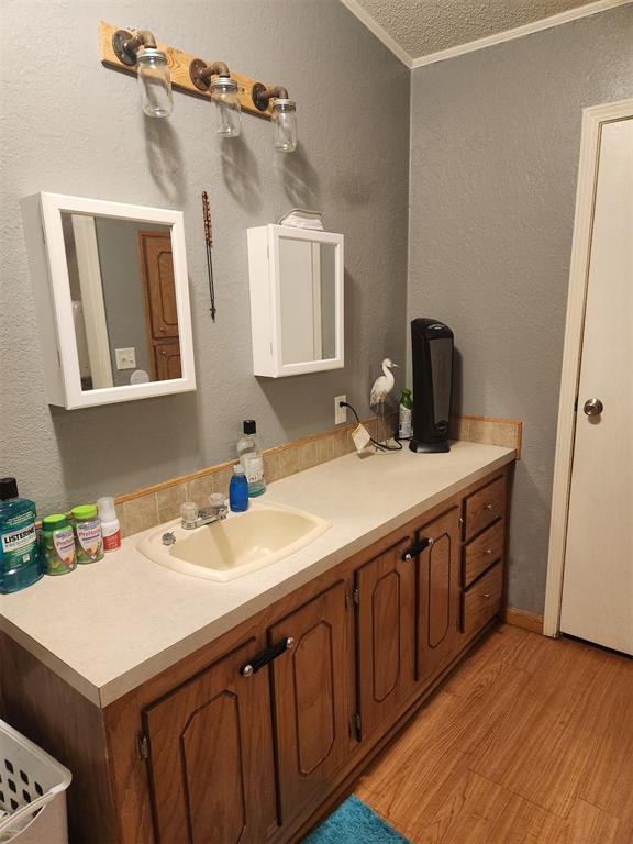 bathroom featuring crown molding, a textured wall, vanity, and wood finished floors