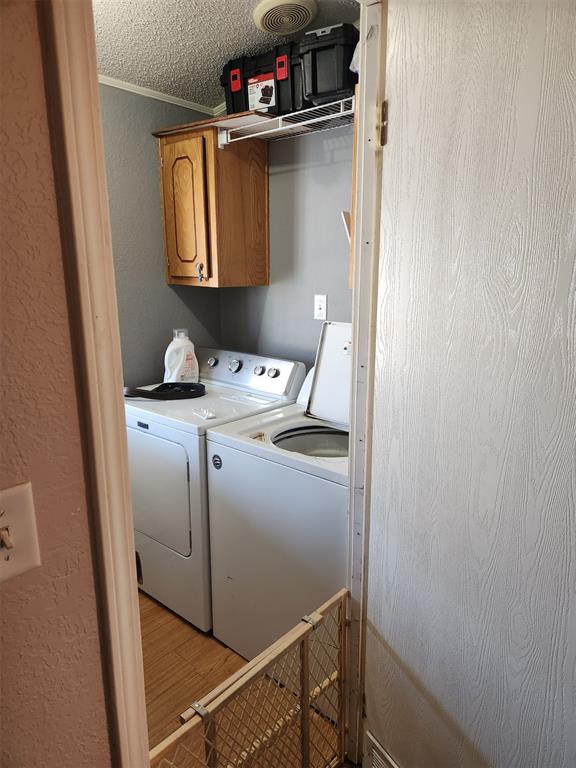 laundry area featuring cabinet space, light wood-style flooring, a textured ceiling, crown molding, and washing machine and dryer